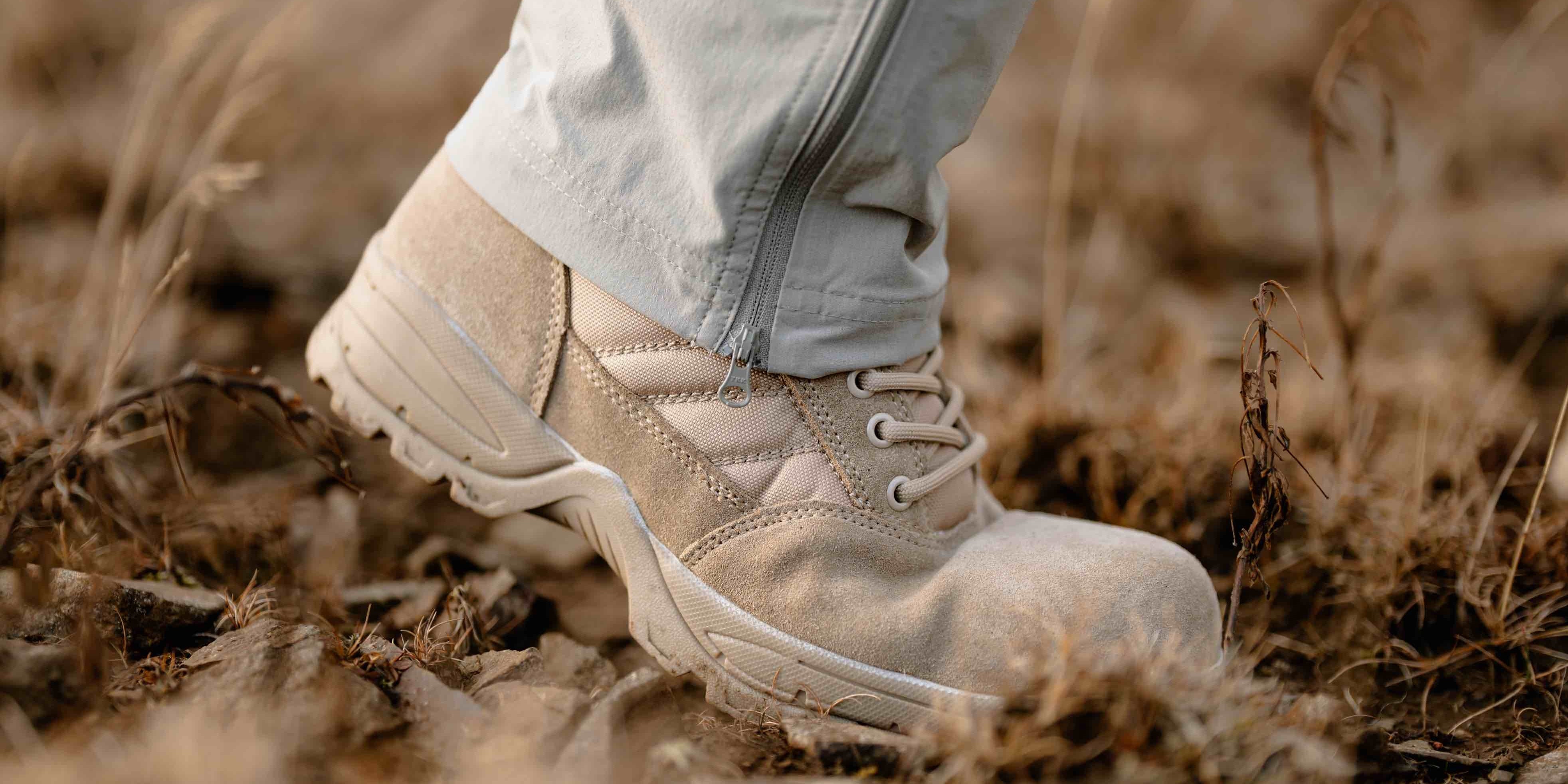 Desert tan military boot walking through dry leaves and brush in a rugged outdoor environment