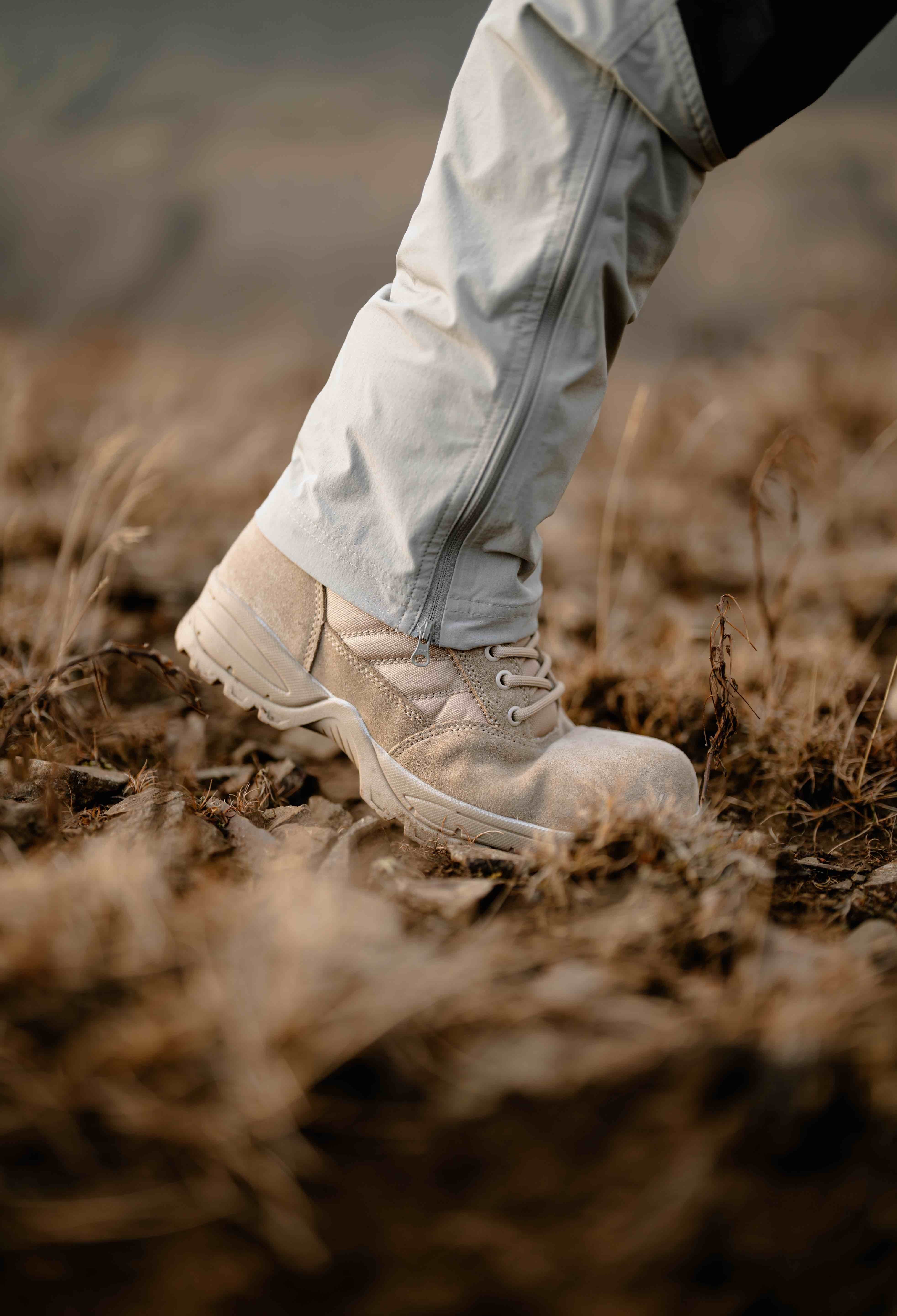 Desert tan military boot walking through dry leaves and brush in a rugged outdoor environment