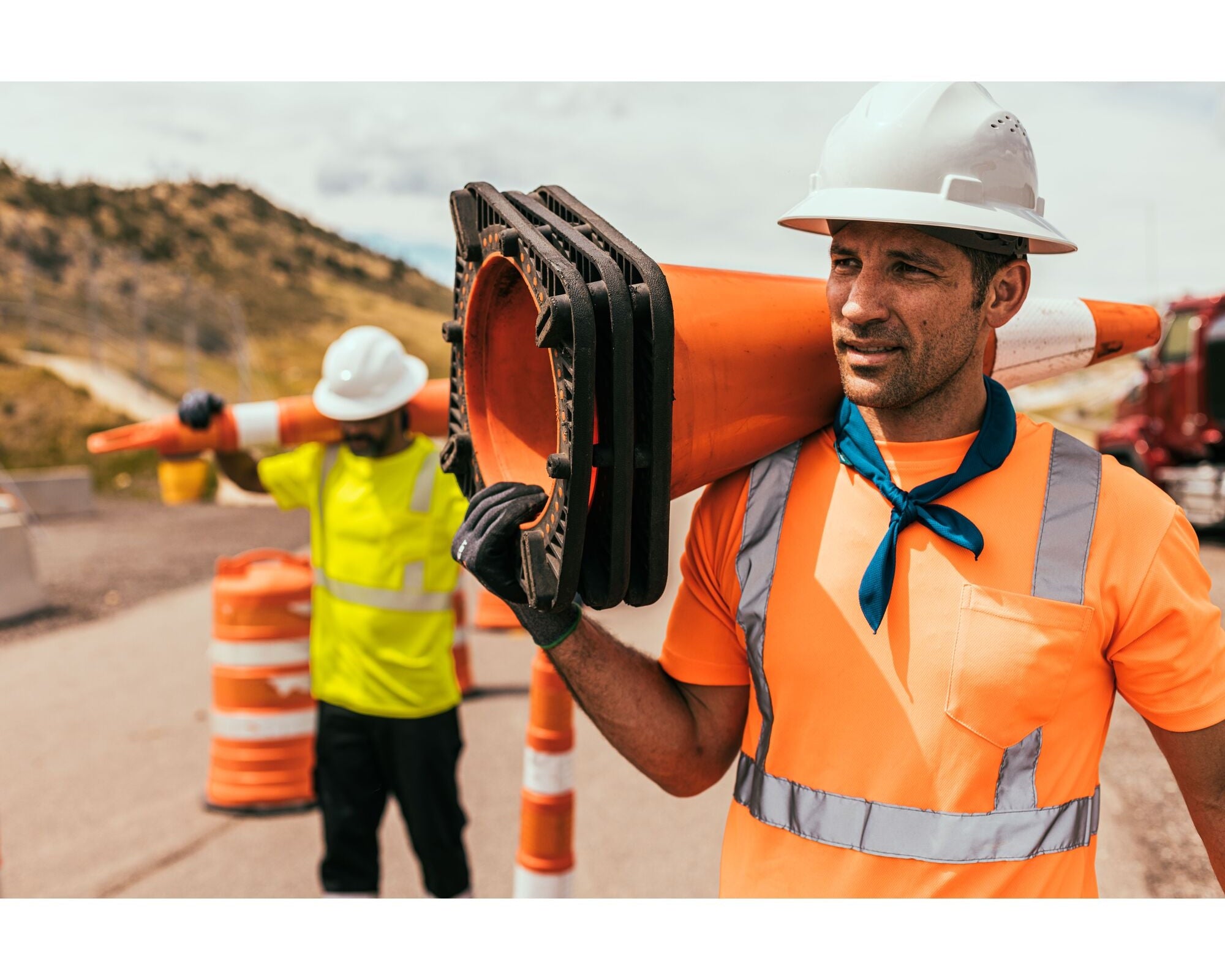 workmen wearing orange and yellow hi-vis t-shirts carrying cones to work