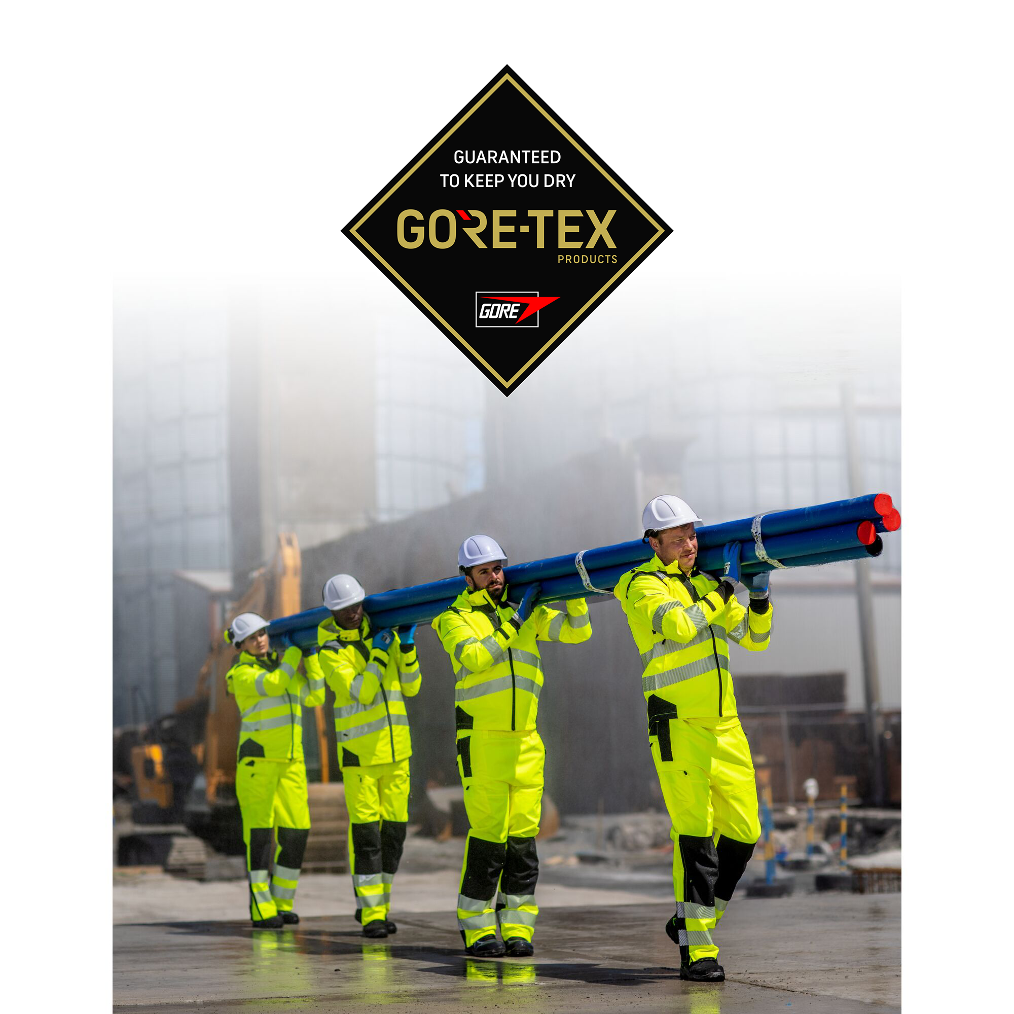 Four construction workers carrying blue industrial pipes while wearing high-visibility yellow waterproof GORE-TEX workwear and white safety helmets on a wet construction site. A GORE-TEX logo above them states “Guaranteed to keep you dry.” By MAK Boots & Garments.